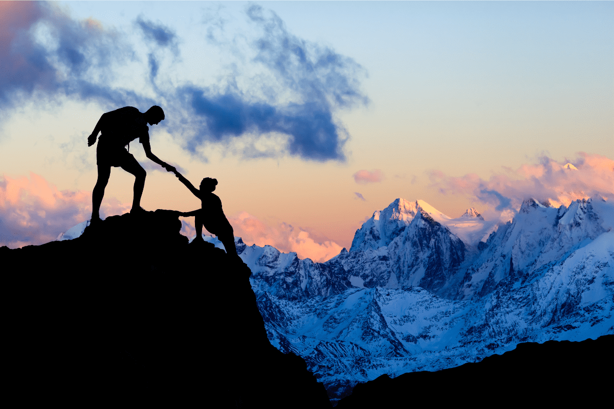 two people helping each climb to the top of a mountain