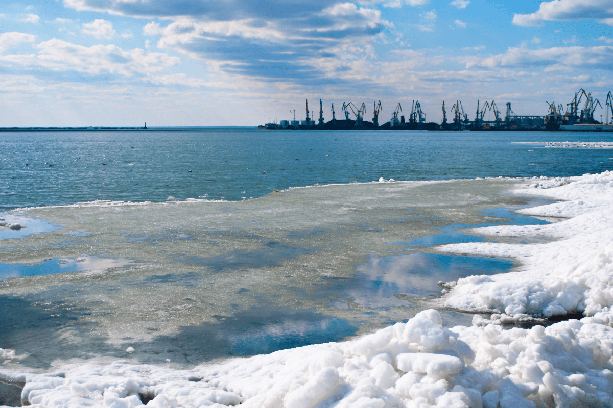 A coast with snow and ice and cranes on an opposite coast in the distant