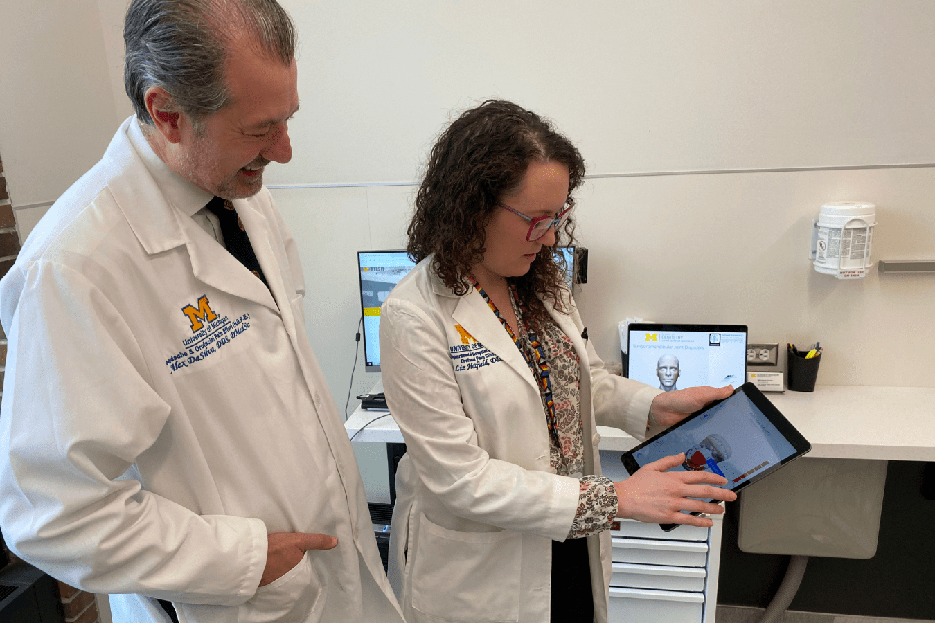 Alexandre DaSilva and Liz Hatfield in lab coats looking at a tablet.